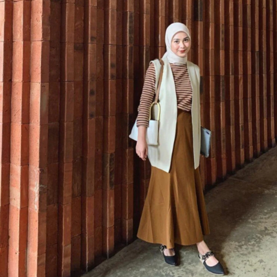 Selebgram hijab Dianty berdiri mengenakan baju motif stripes dan rok panjang warna cokelat dengan blazer dan hijab warna krem. l Instagram/diantyy.a